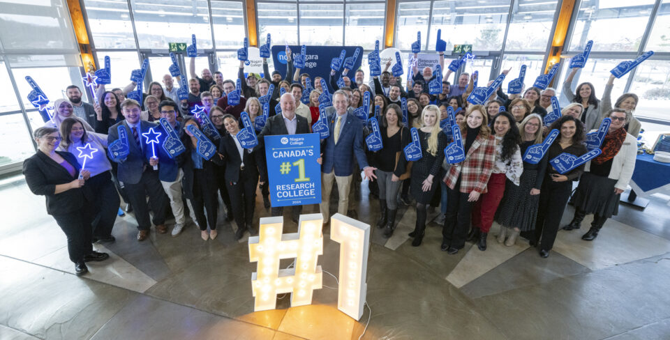 http://Group%20photo%20of%20Niagara%20College%20staff%20with%20foam%20fingers%20and%20posters%20declaring%20status%20as%20#1