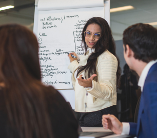 Three Student business research assistants, one in front of a chart presenting to others.