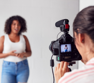 Videographer with camera pointed at woman who is speaking