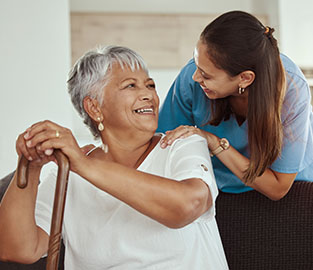 Senior lady holding cane and smiling at a nurse patting her shoulder and smiling
